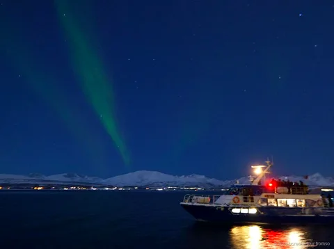 Northern Lights over the fjord seen from the Tromso aurora cruise boat